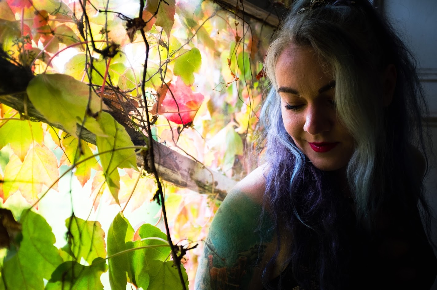 Tattooed girl with blue and white hair sitting by an ivy coloured window